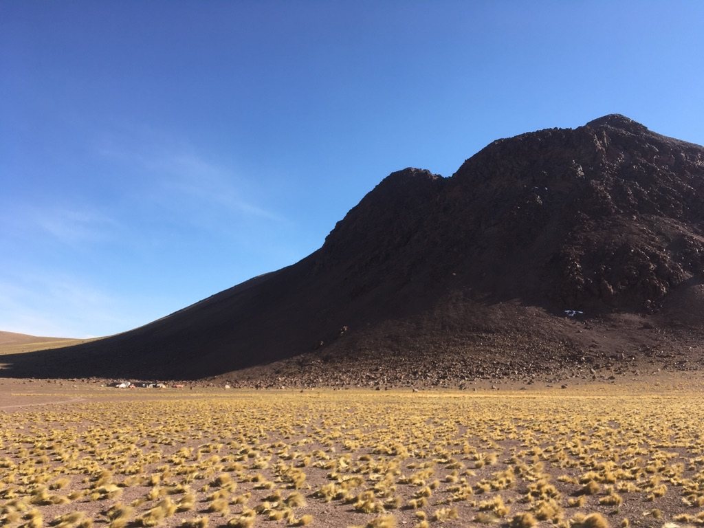 Dark volcanic cone rising above golden grassland