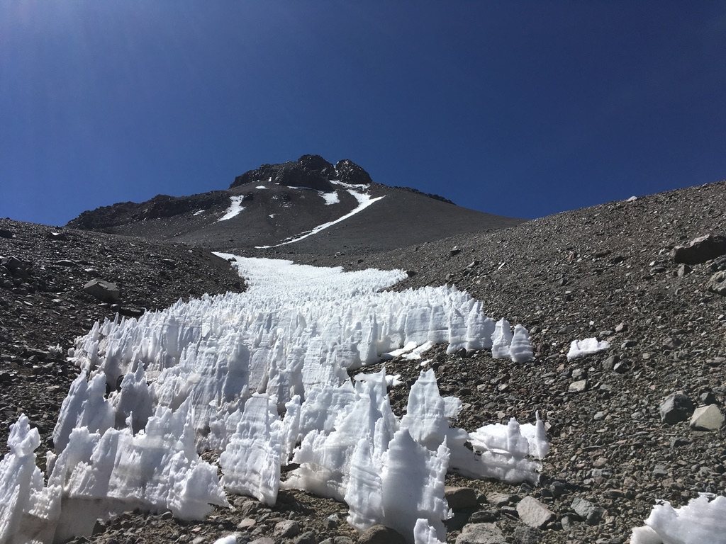 Field of white penitentes ice blades below a dark volcanic peak