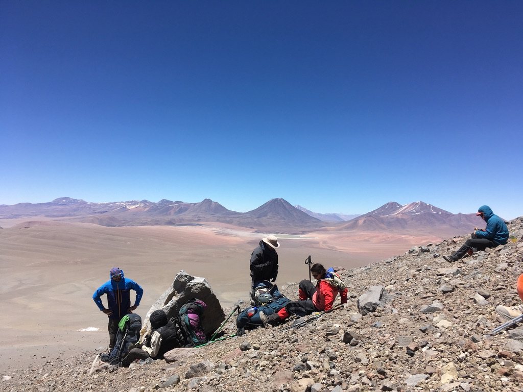 Field team with packs resting on a rocky slope above a wide basin