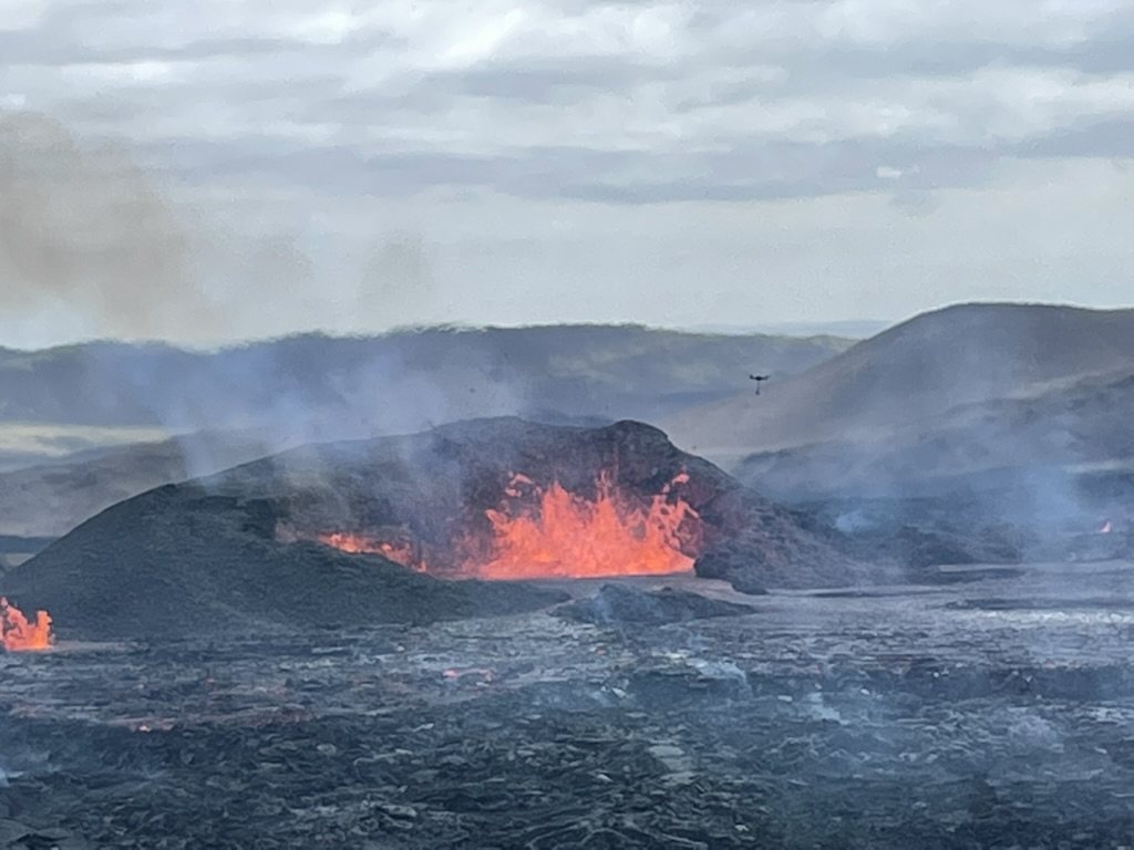 Spatter cone with glowing lava beneath grey skies