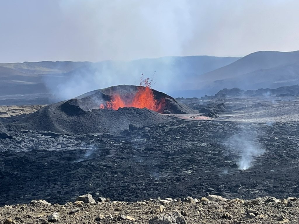 Lava fountaining from a spatter cone across a black lava field