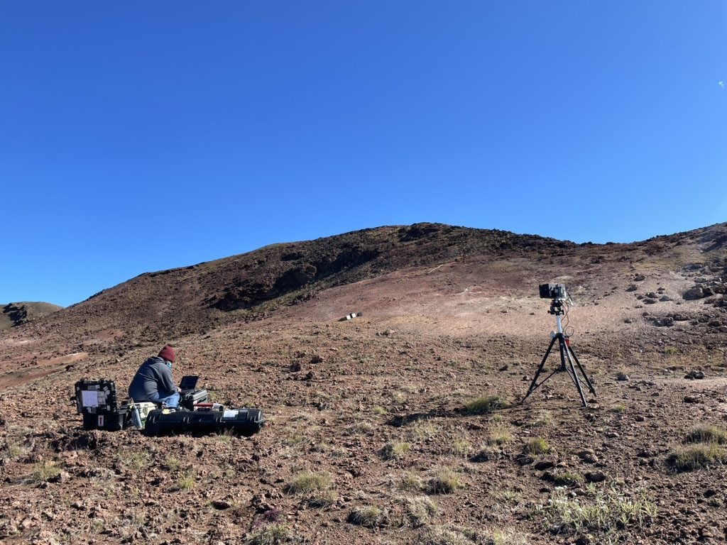 Field station with equipment cases and a tripod-mounted camera on a hillside