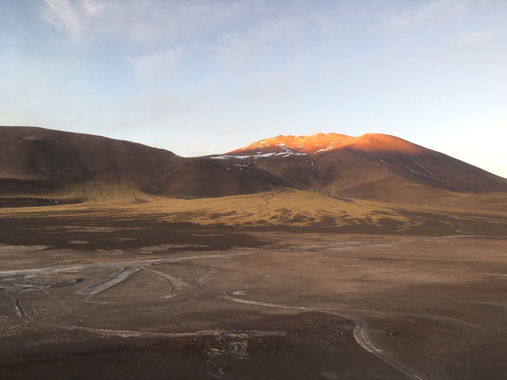 Volcanic summit lit orange by alpenglow above a dark valley