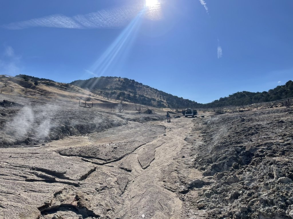 Steam rising from pale altered ground in a valley under bright sun